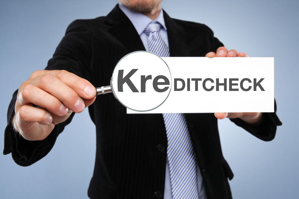 Mann hält Lupe vor einem Schild mit der Aufschrift 'Kreditcheck' Kredite vergleichen